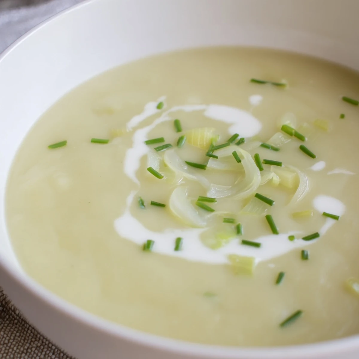 Creamy Leek and Potato Soup swirled with fresh chives in a rustic white bowl, steam rising from the velvety texture.  