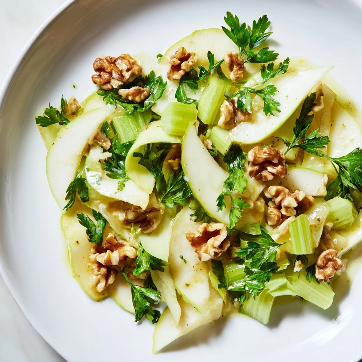 Crunchy walnuts and tender greens glisten with tangy vinaigrette in this refreshing Apple and Celery Salad with Walnuts served in a white bowl.