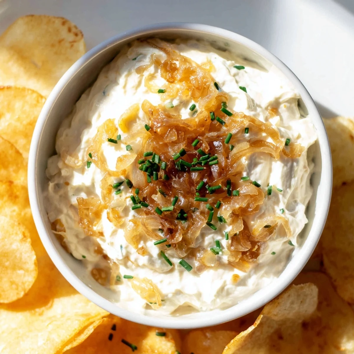 Homemade onion dip with caramelized yellow onions and sour cream, served in a white ceramic dish with a handful of crunchy chips.  