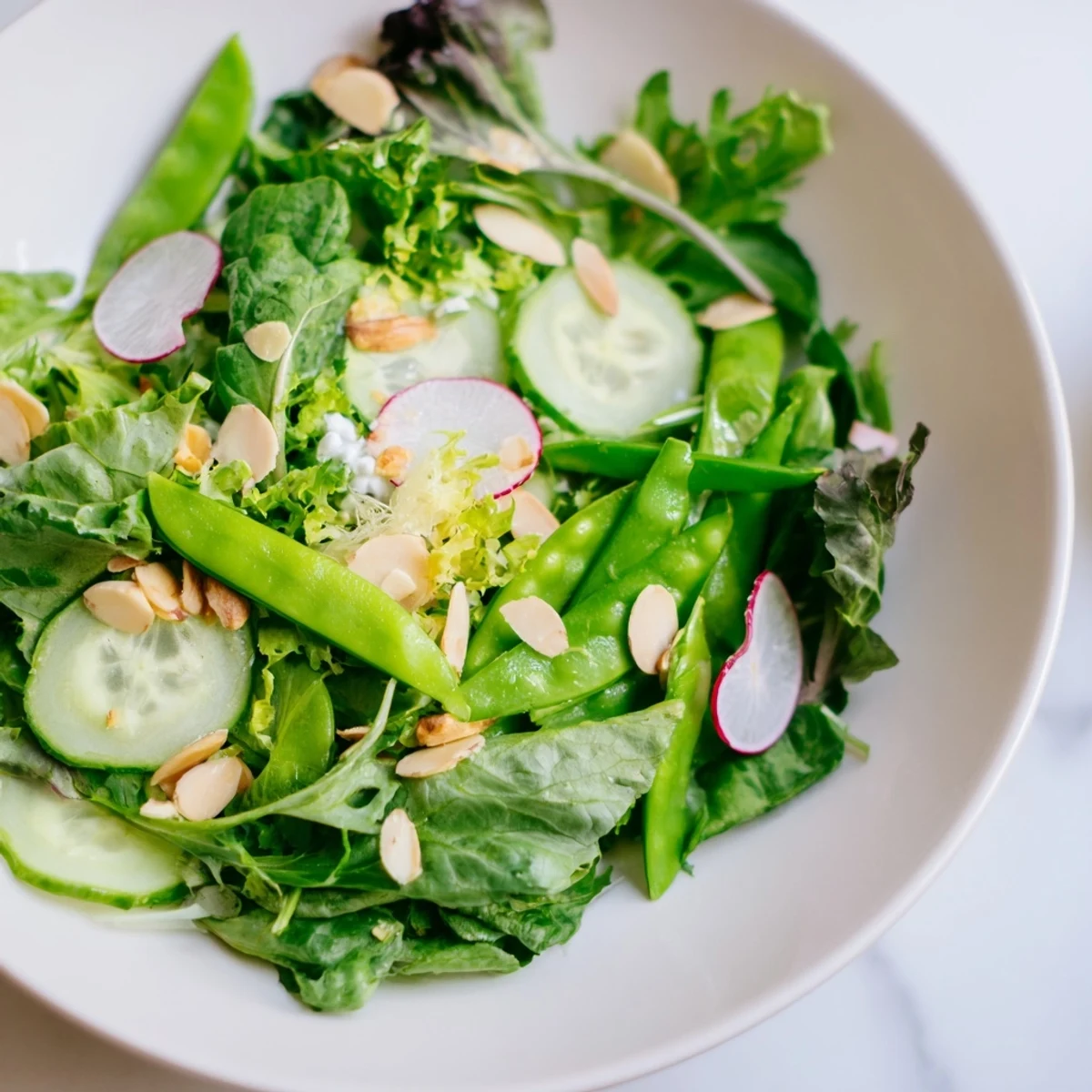 Vibrant Spring Greens Salad with Lemon Vinaigrette arranged in a white bowl, featuring crisp greens and vegetables for a light, refreshing side.  