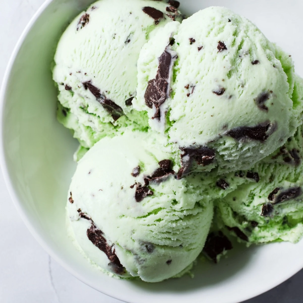 Green Mint Chocolate Chip Ice Cream frozen in a vintage tin container, showing its rich, creamy texture and flecks of chocolate.
