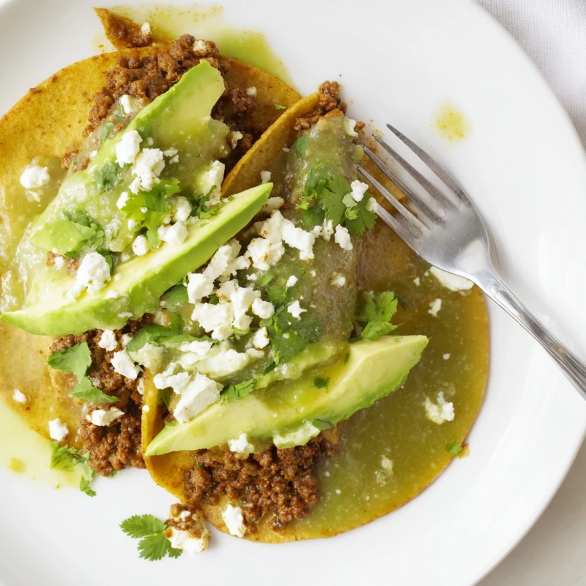 Fresh tomatillo salsa verde and avocado slices garnish these homemade spicy beef tacos, creating a vibrant Mexican-inspired dinner.  