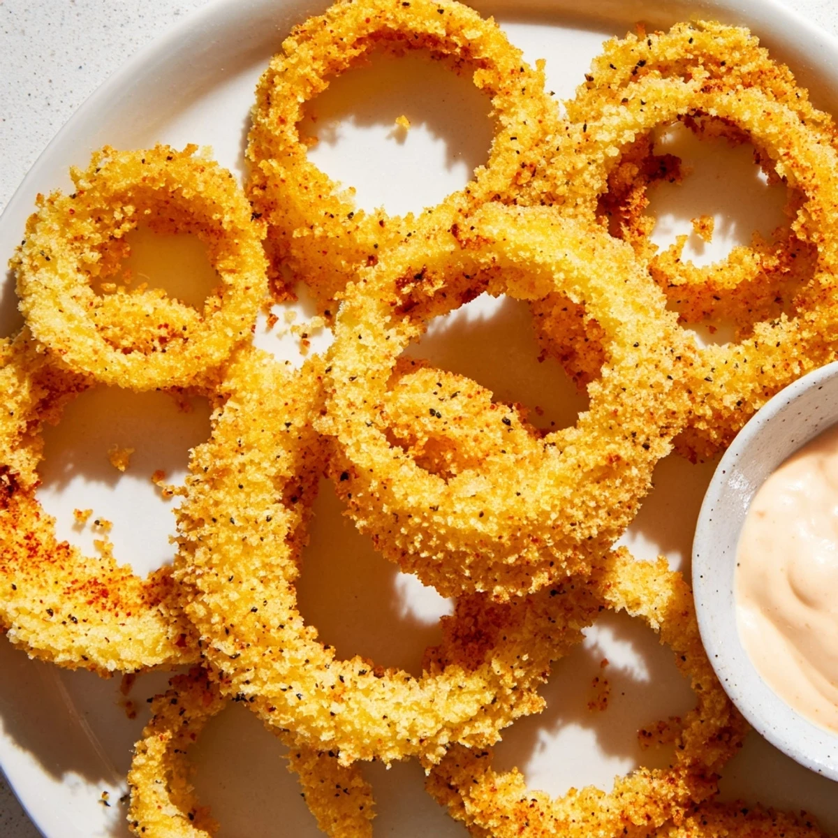 Crispy Air Fryer Onion Rings with Dip stacked high on a plate with creamy sauce, golden brown and crunchy.