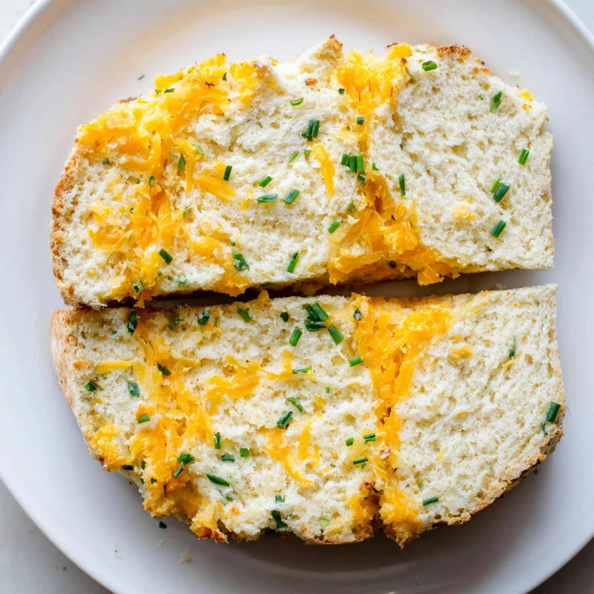 Freshly baked Savory Cheddar & Chive Irish Soda Bread resting on a cooling rack, showcasing a deep golden-brown crust cut with a traditional cross on top.