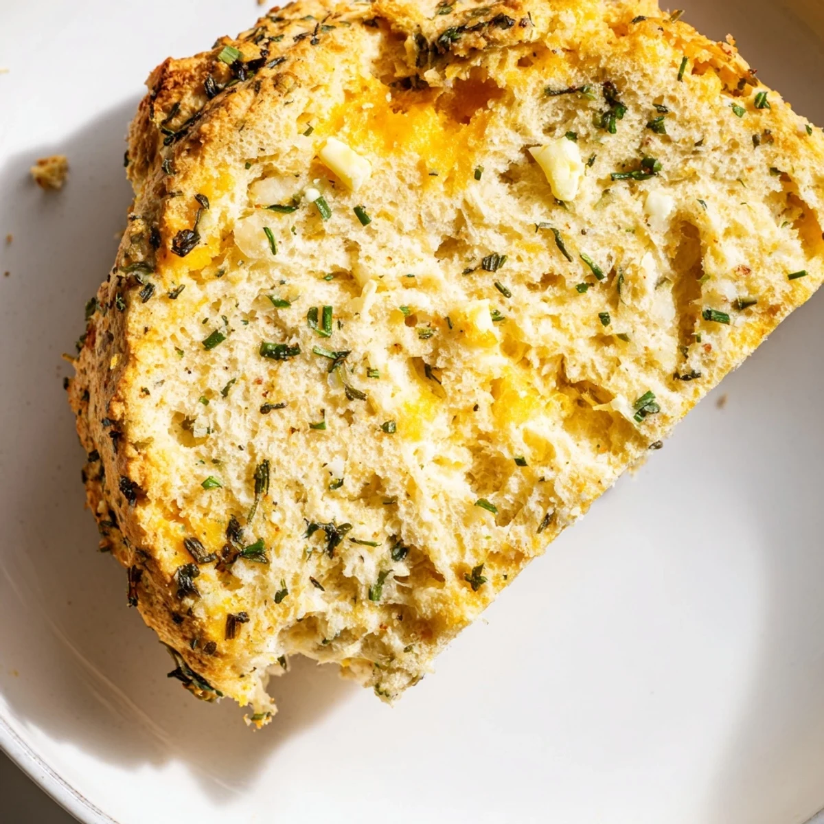 A rustic slice of Savory Herbed Cheddar Irish Soda Bread sits beside a warm bowl of creamy tomato soup for a comforting lunch.