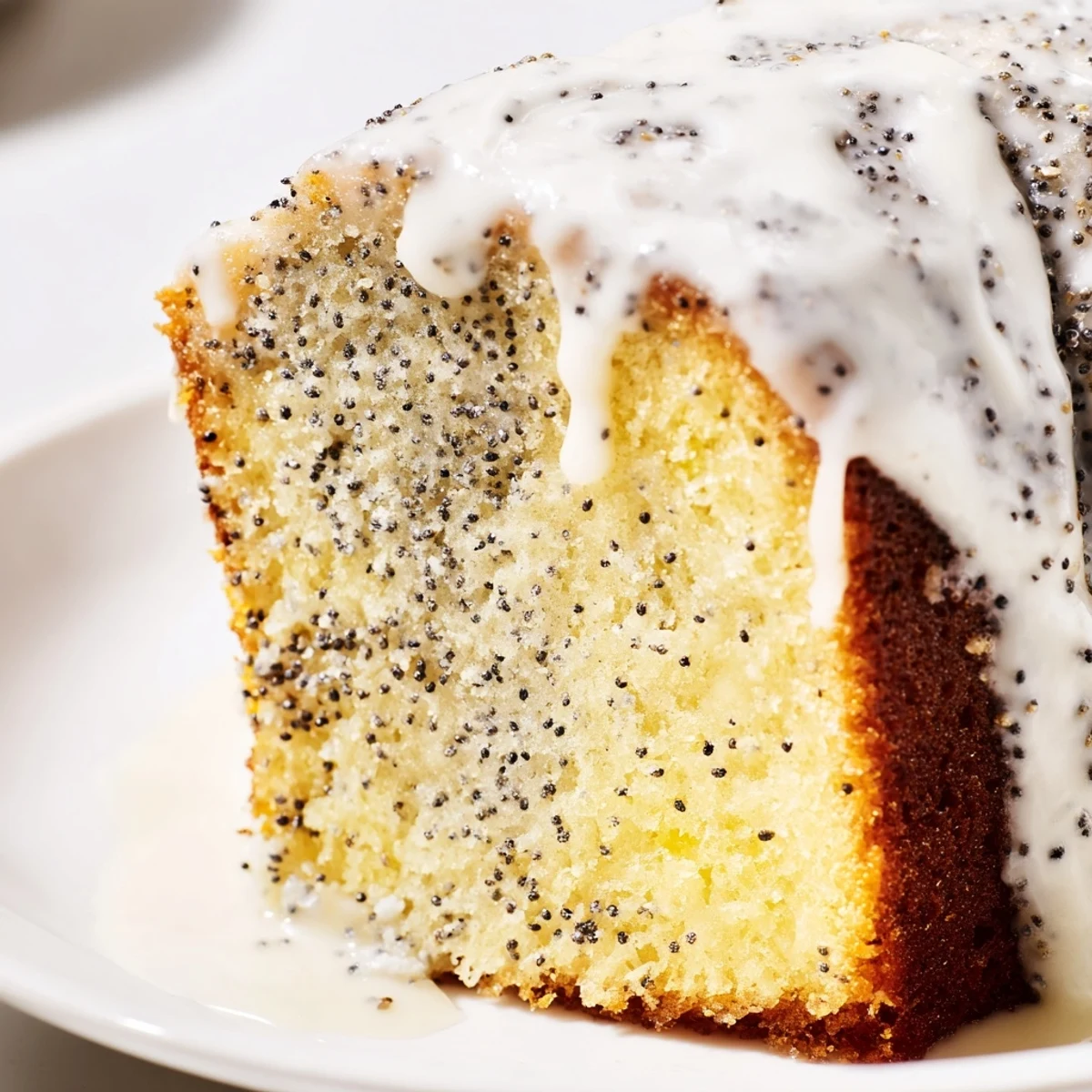 Glazed Lemon Poppy Seed Cake on a white plate with fresh lemon slices and tea nearby.