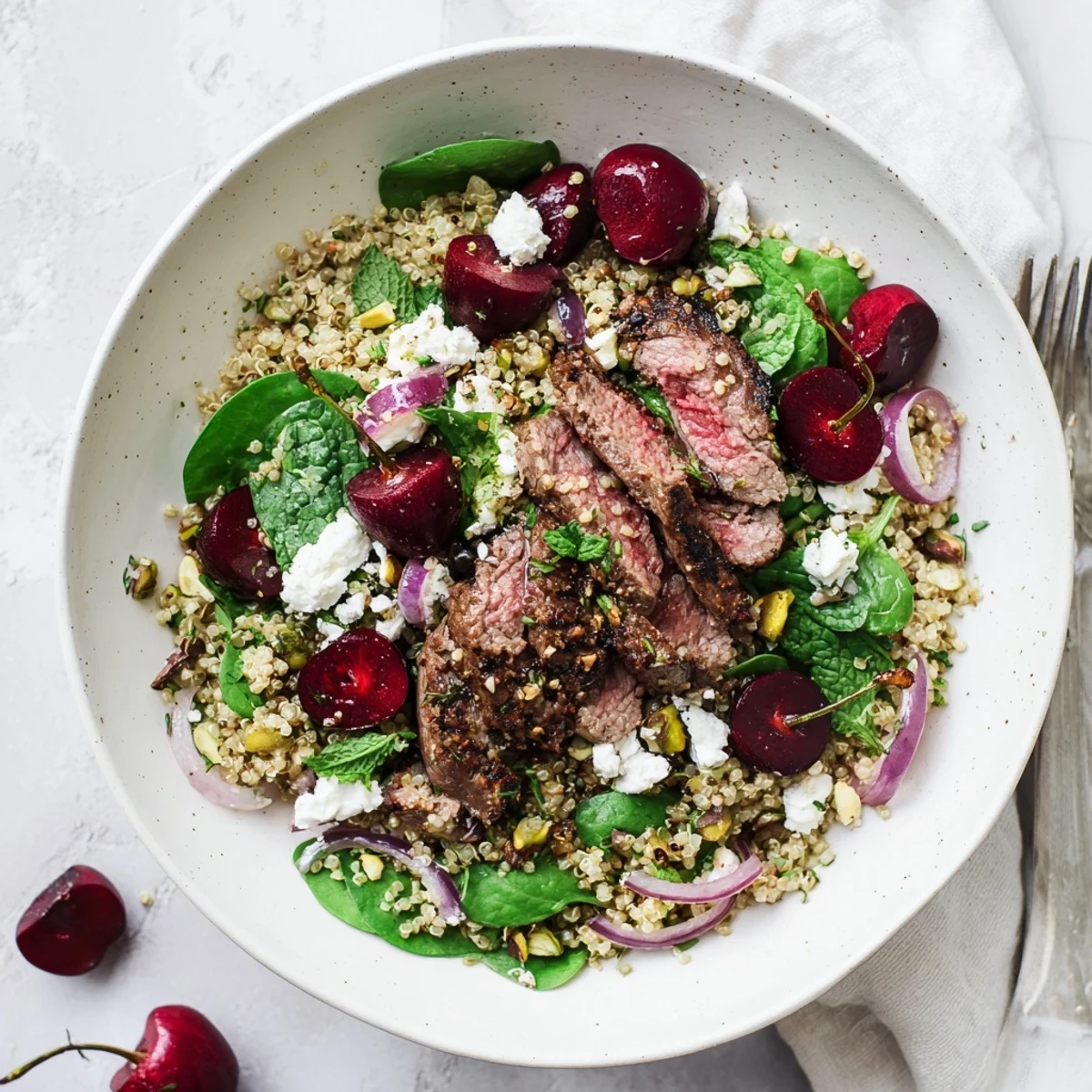 Colorful bowl of cherry quinoa salad with tender spiced lamb slices and fresh herbs