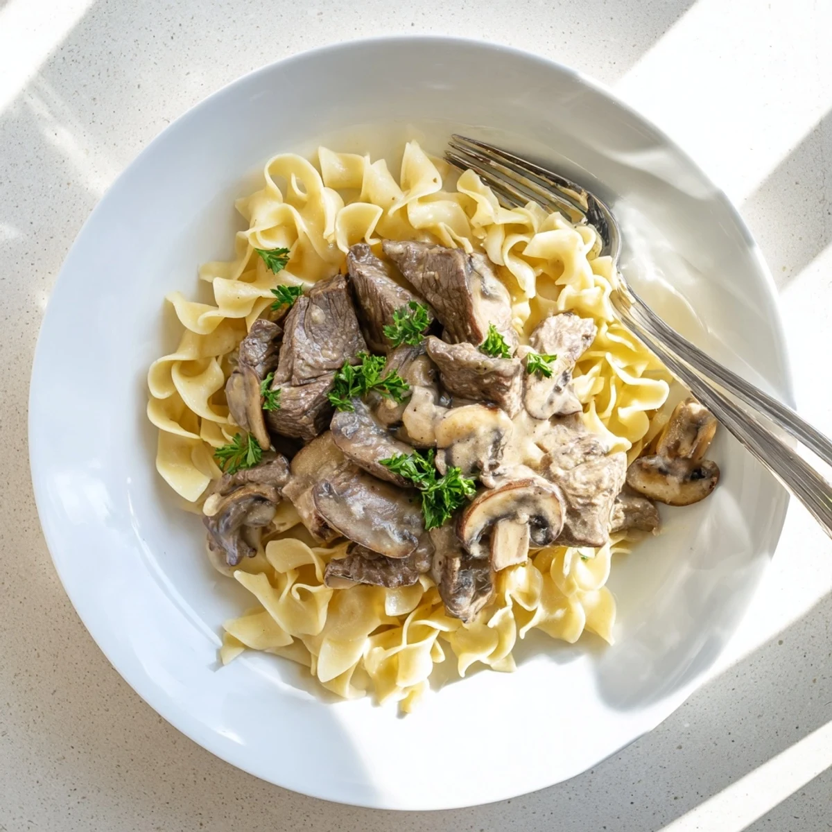 Homemade beef and mushroom stroganoff plated on white pasta with chopped parsley topping
