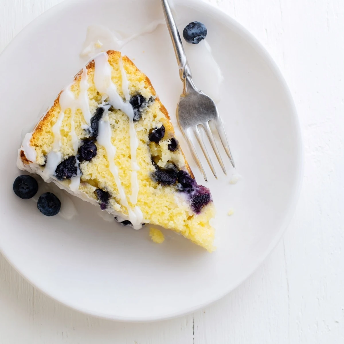 Moist lemon blueberry cake slice showcasing scattered blueberries and bright lemon zest garnish