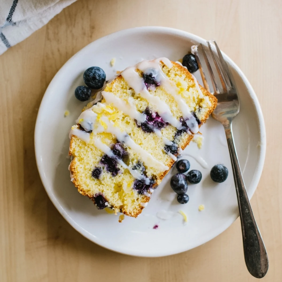 Freshly baked lemon blueberry cake with glossy lemon icing on a white cake stand