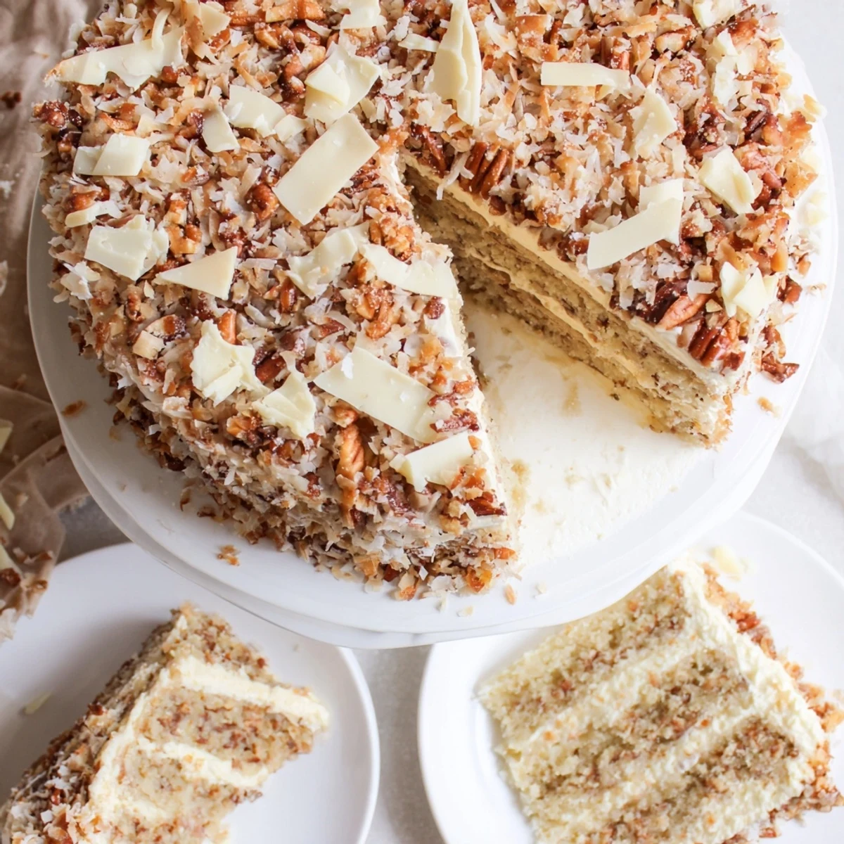 Slice of white German chocolate cake showing fluffy white cake topped with golden coconut and toasted pecan frosting