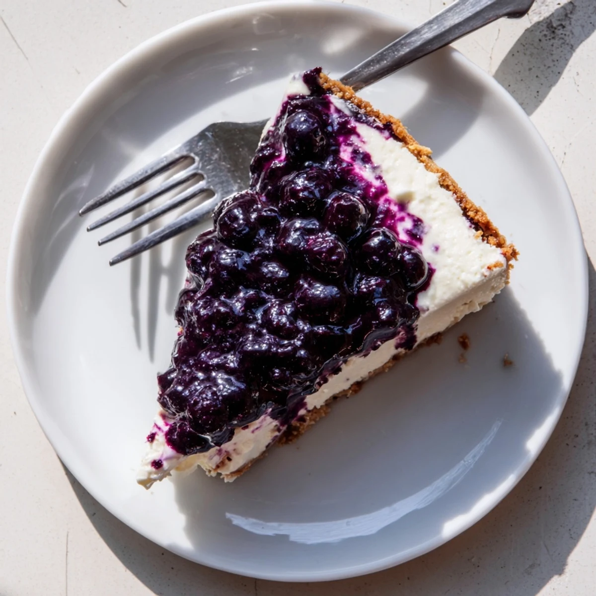 Rich blueberry cheesecake plated on white dish with swirled berry sauce and buttery golden base