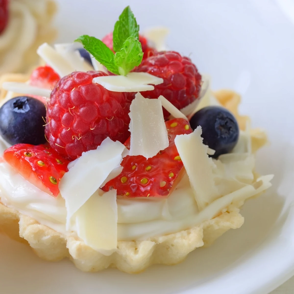 Golden white chocolate mousse tartlets topped with fresh raspberries and blueberries on white plate
