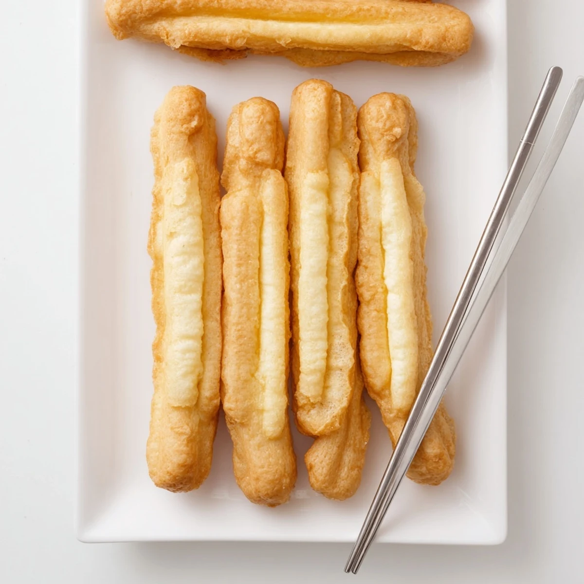 Freshly fried golden-brown Youtiao pastry sticks arranged on a wire rack after deep frying