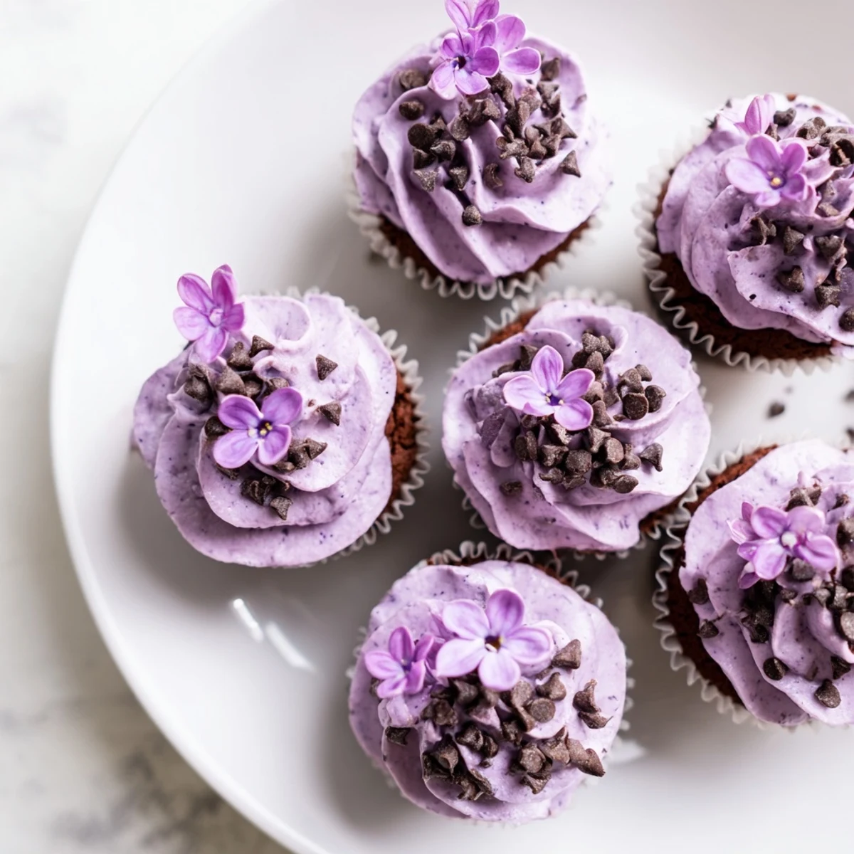 Rich chocolate lilac cupcakes decorated with fresh flowers on a rustic wooden board