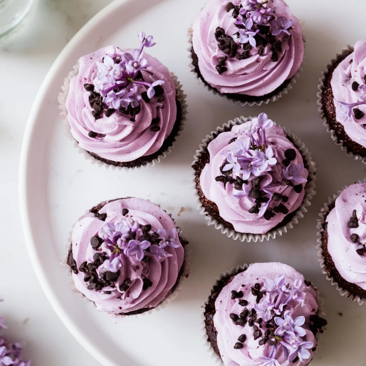 Six floral lilac chocolate cupcakes with lilac buttercream frosting and fresh blossom garnish