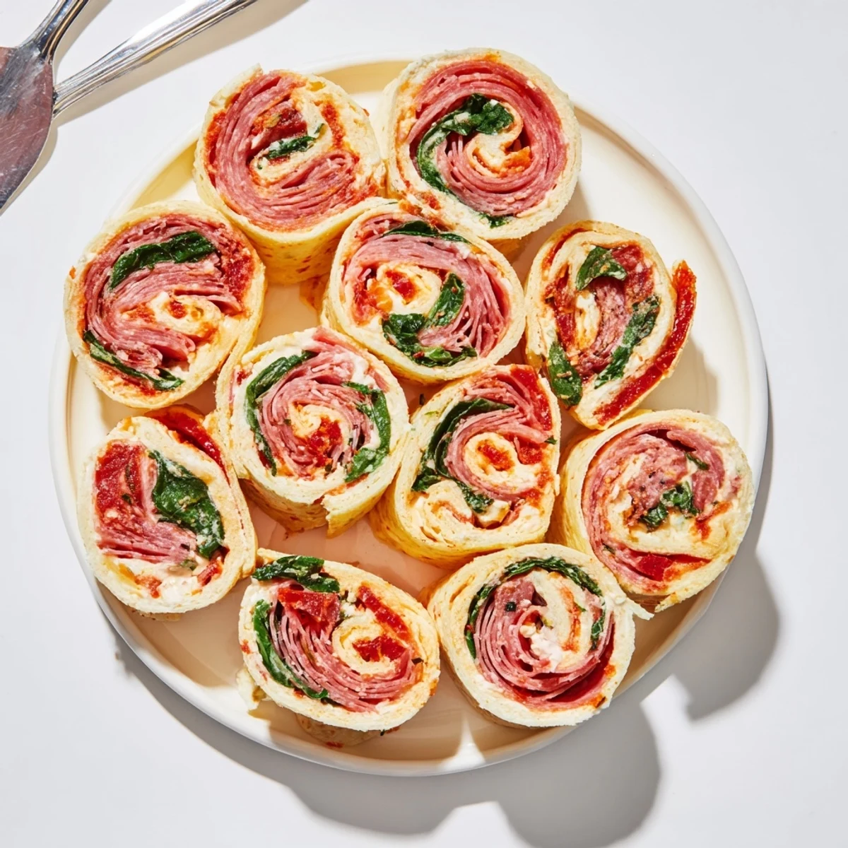 Cross-cut view of savory Italian pinwheels revealing spiral pattern of roasted red pepper cream cheese, pepperoni, and provolone cheese