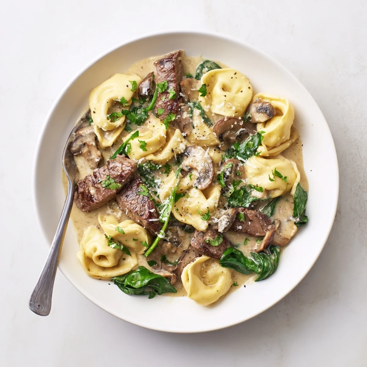 Savory steak strips and cheese tortellini coated in velvety garlic cream sauce with parsley garnish