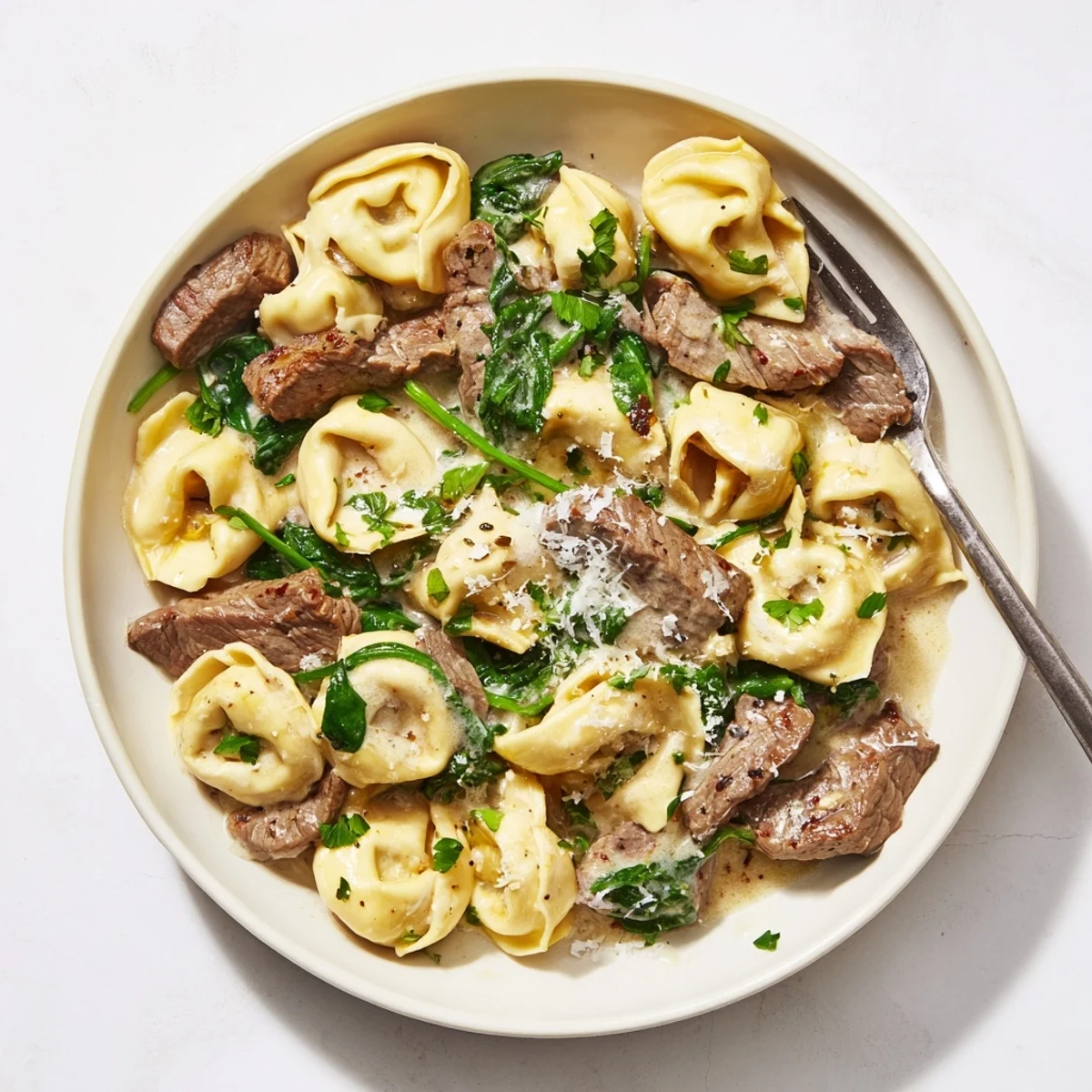 Creamy garlic steak tortellini plated with melted Parmesan, wilted spinach, and fresh parsley sprinkles