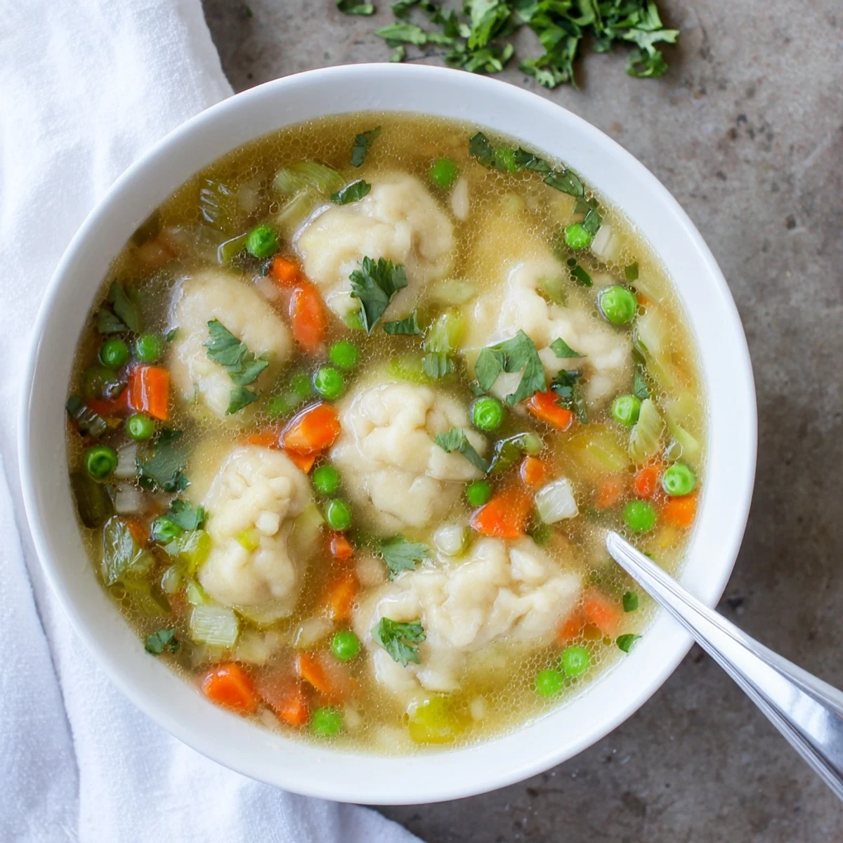 Golden dumpling soup featuring fluffy parsley dumplings floating in vegetable broth with carrots celery and peas