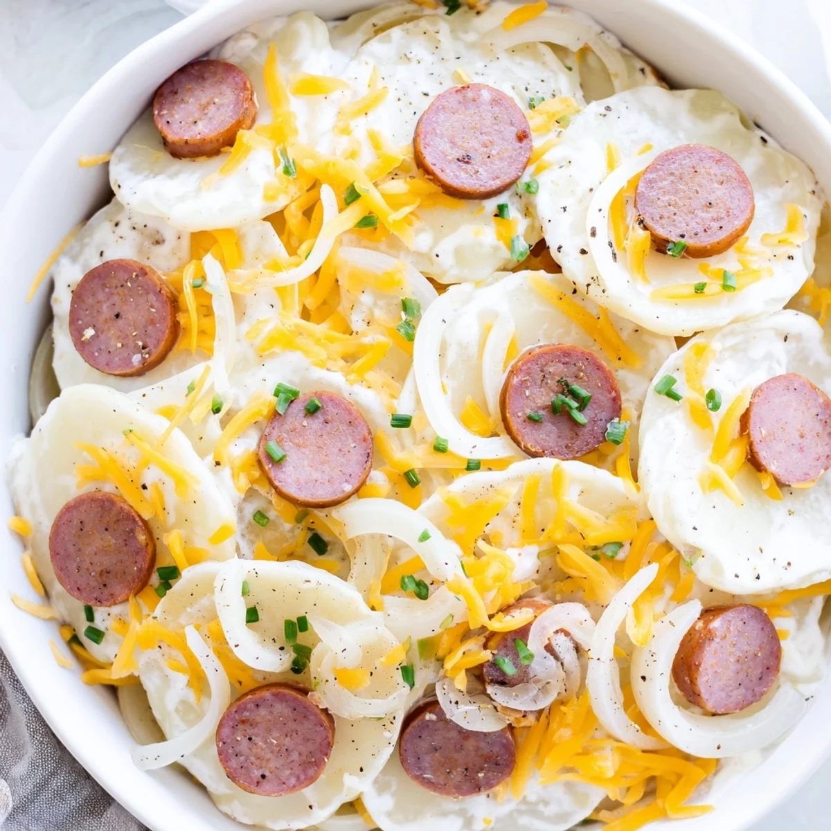 Hearty pierogi and kielbasa casserole with gooey cheese topping garnished with fresh chives