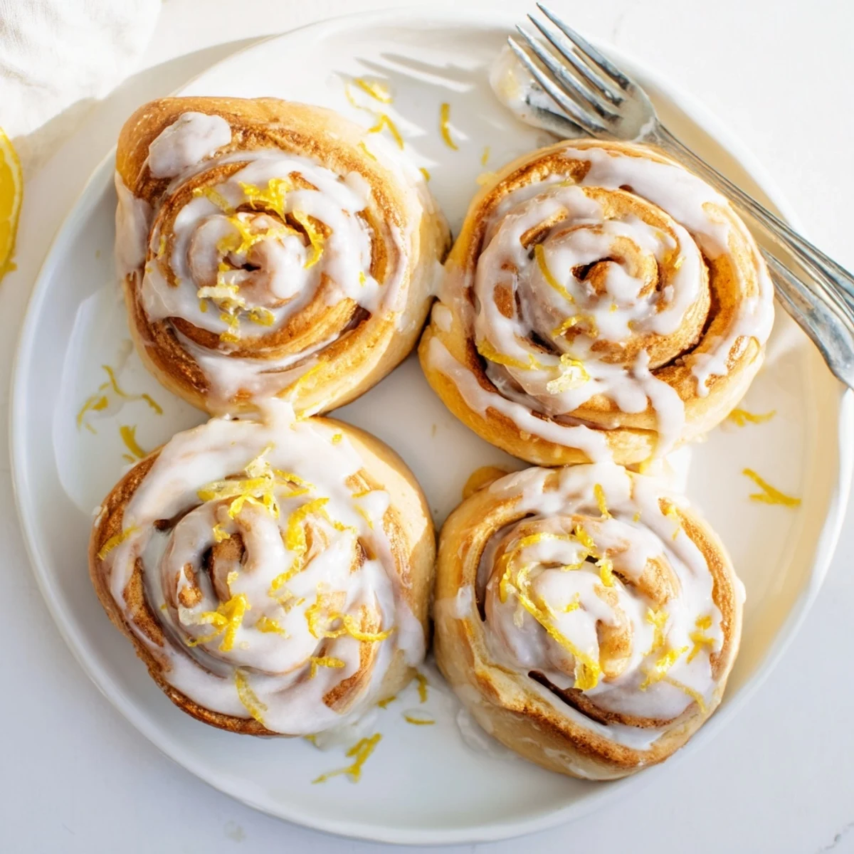 Golden homemade lemon rolls drizzled with white tangy glaze on a white ceramic plate