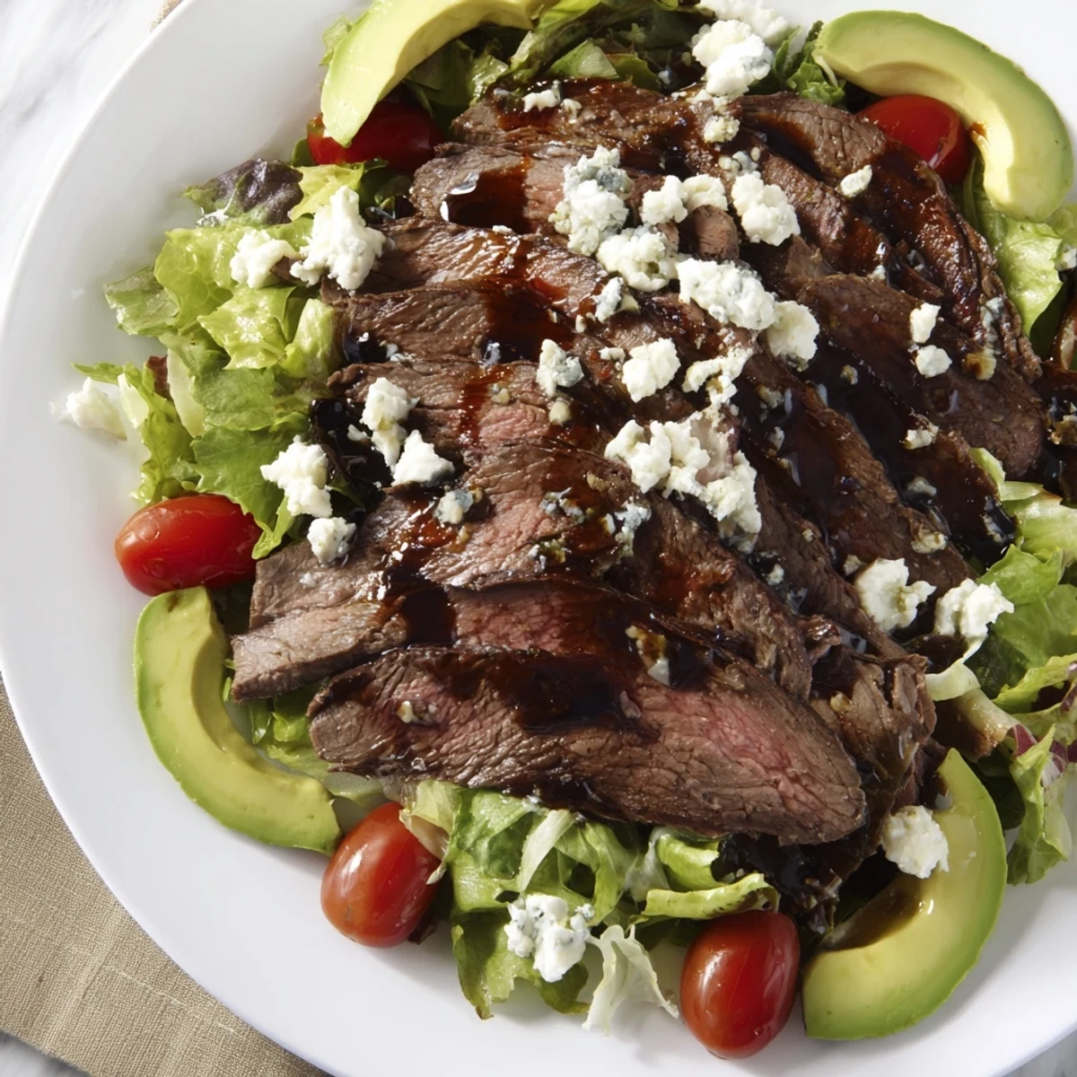 Sliced balsamic steak arranged over crisp greens in a balsamic steak Gorgonzola salad with grilled corn