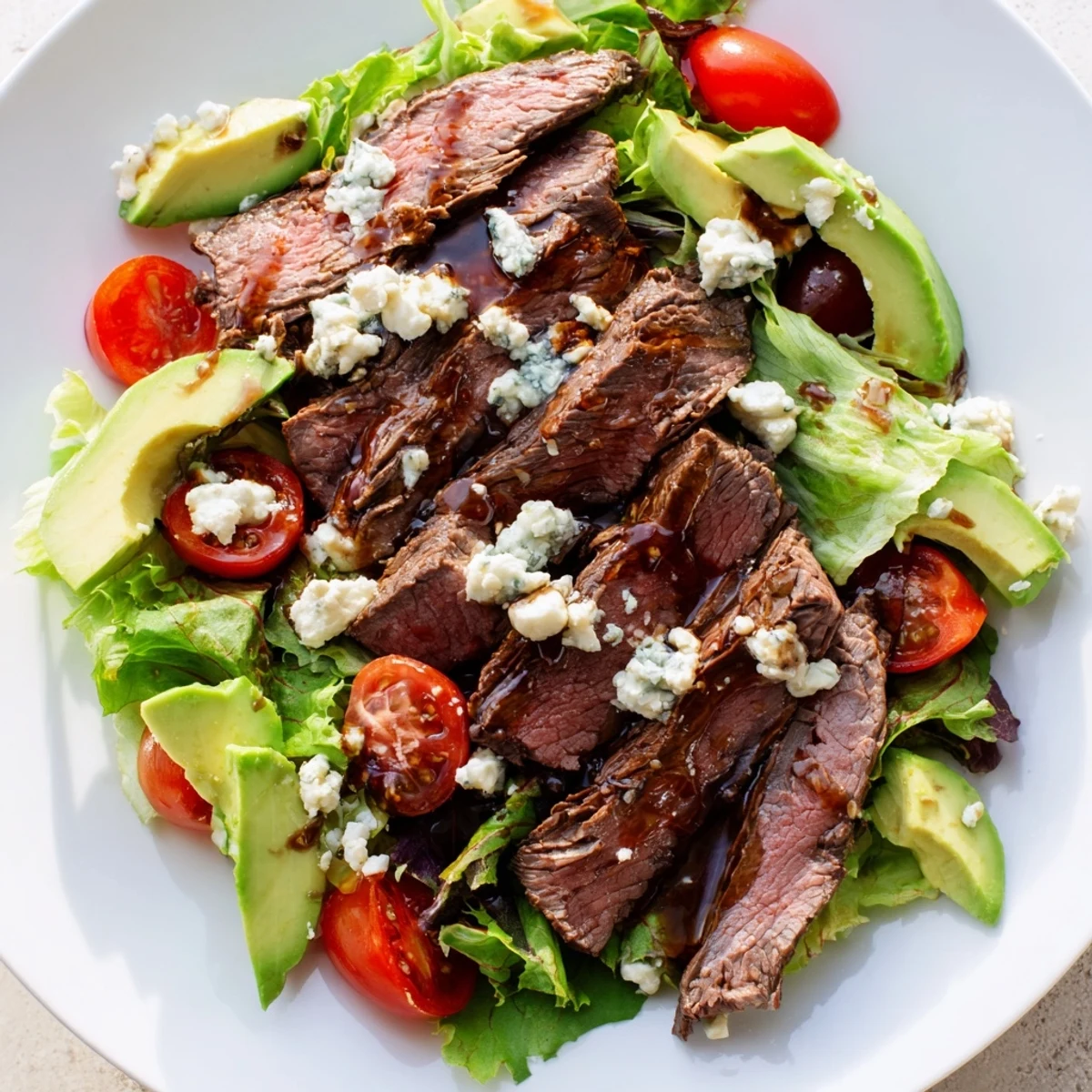 A vibrant balsamic steak Gorgonzola salad with grilled corn drizzled with vinaigrette on a white platter