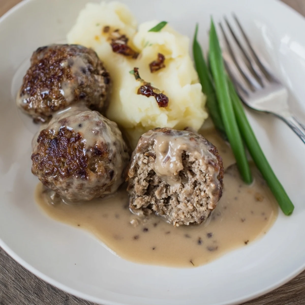 Plate of Homemade Ikea Meatballs browned golden, sauce glistening, lingonberry on side