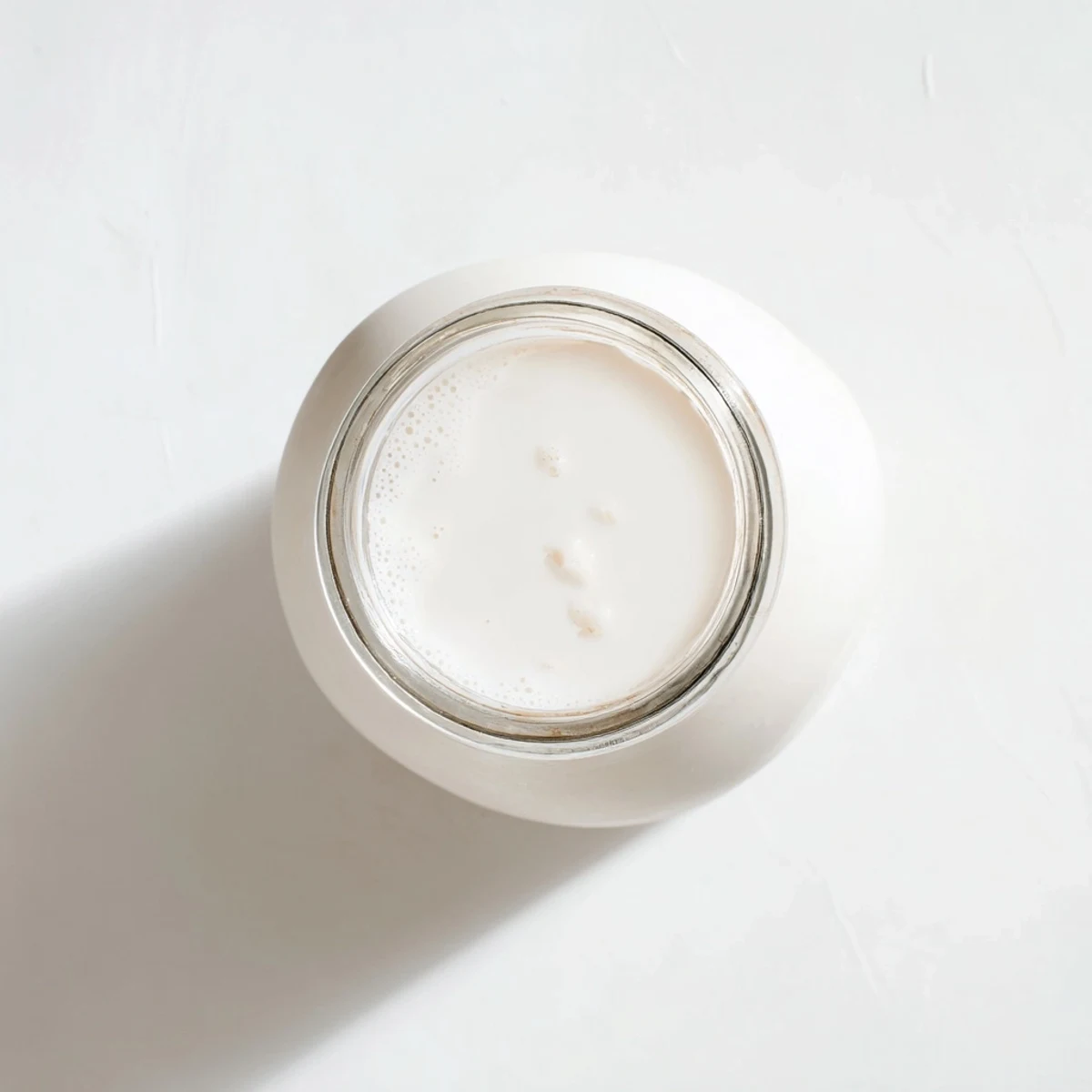 Homemade coconut milk in clear glass bottle alongside shredded coconut, creamy white liquid