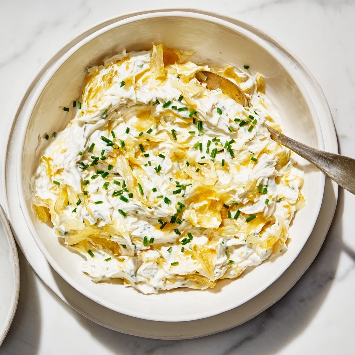 Creamy French onion dip topped with golden caramelized onions and fresh chives in a white serving bowl