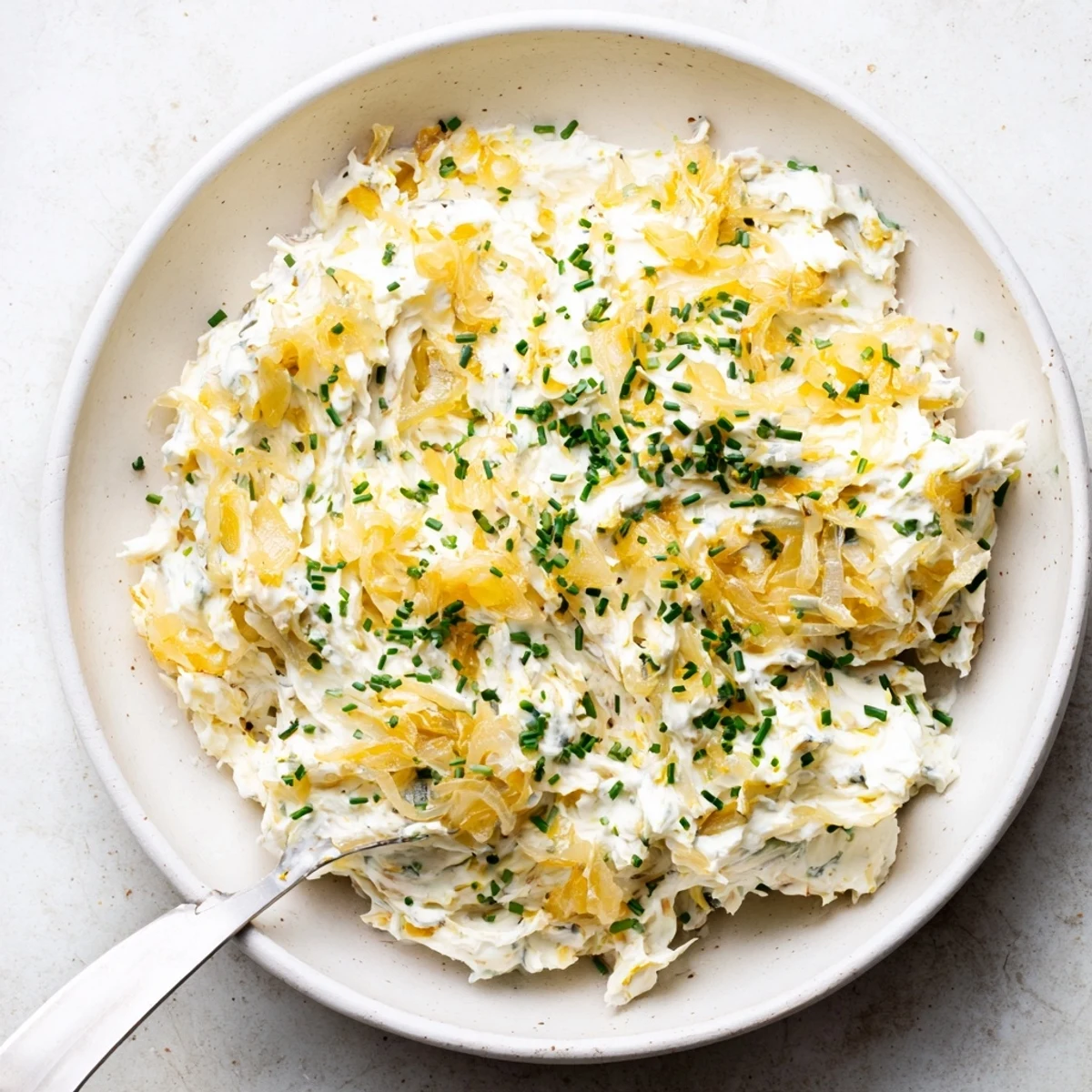 Bowl of savory French onion dip garnished with green onions alongside pretzels and fresh sliced vegetables