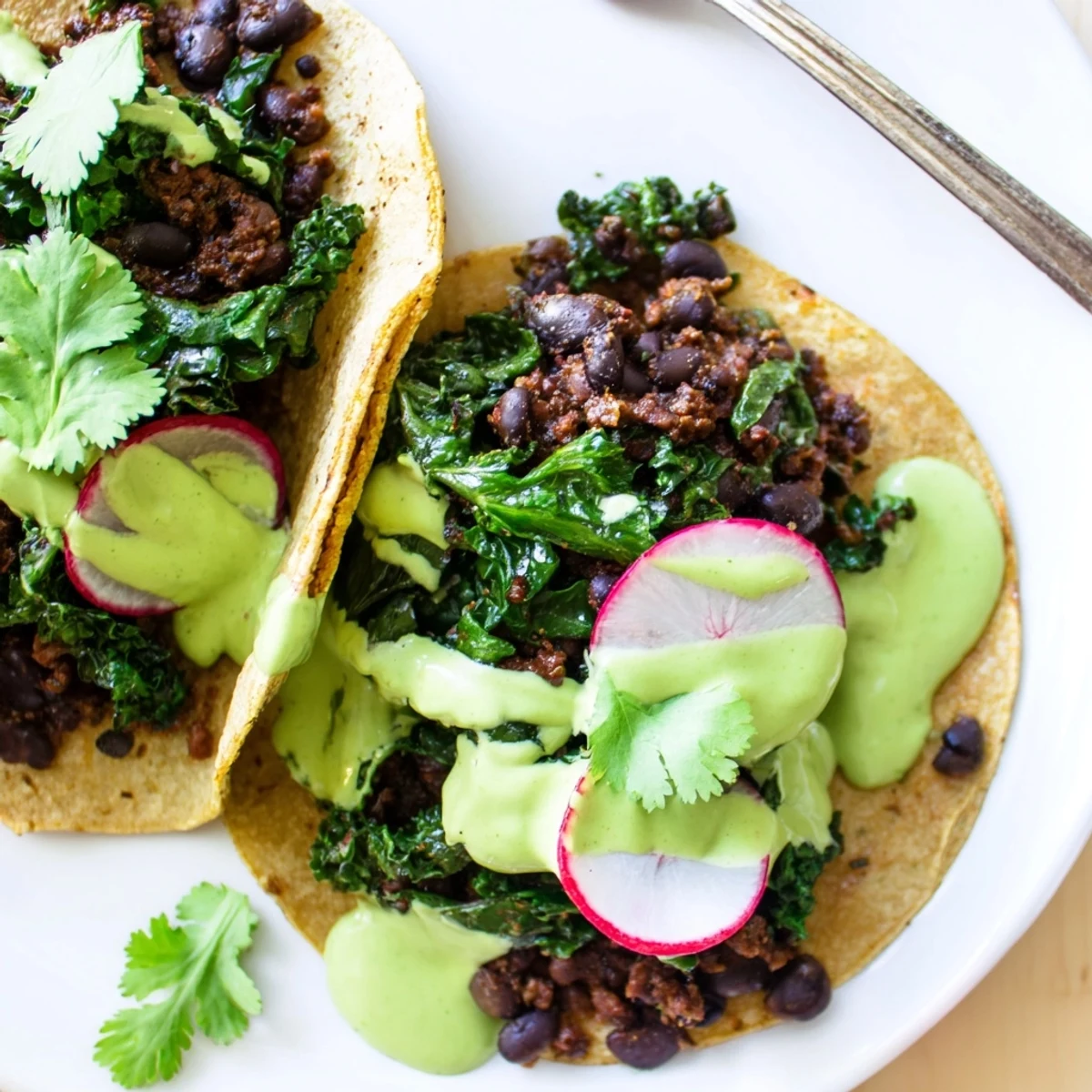 Smoky black bean kale tacos drizzled with vibrant green sauce on warm tortillas