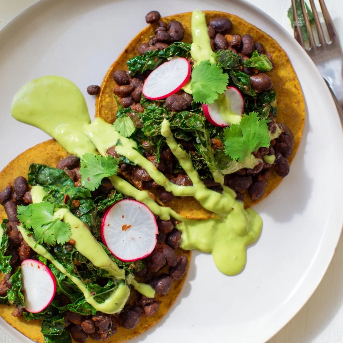 Warm tortillas loaded with smoky black beans kale and creamy avocado green sauce