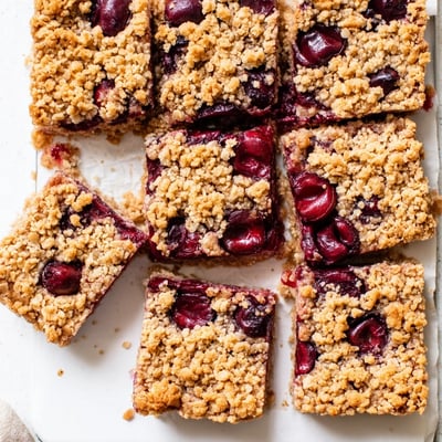 A close-up shot of Easy Tasty Cherry Crumble Bars on a rustic wooden table, with vanilla ice cream melting beside them.
