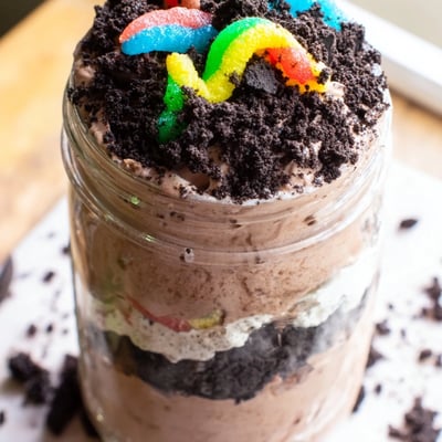 Crushed cookie crumbs top this rich dirt pudding dessert with crawling gummy worms