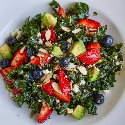 Vibrant summer kale salad drizzled with lemon-honey vinaigrette beside sliced strawberries and avocado.